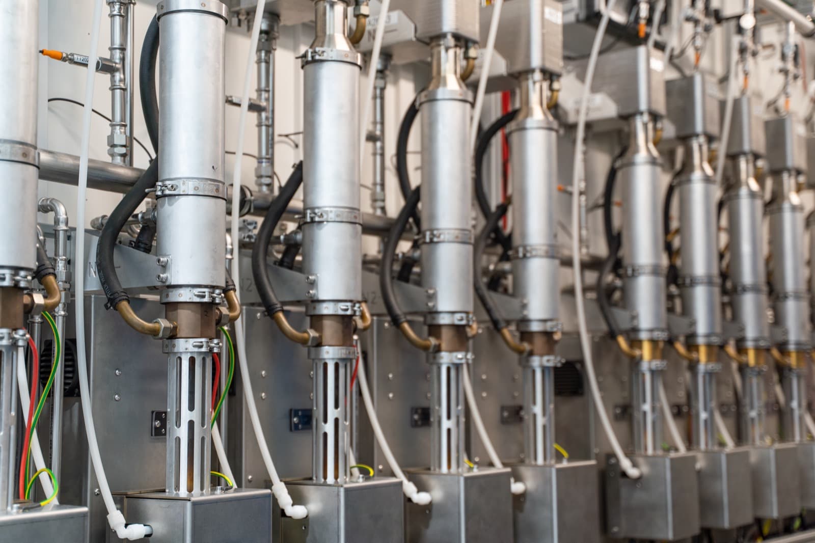 A row of plasma generator cells in stainless steel, each with its own gas and coolant lines, repeating down the length of the rack