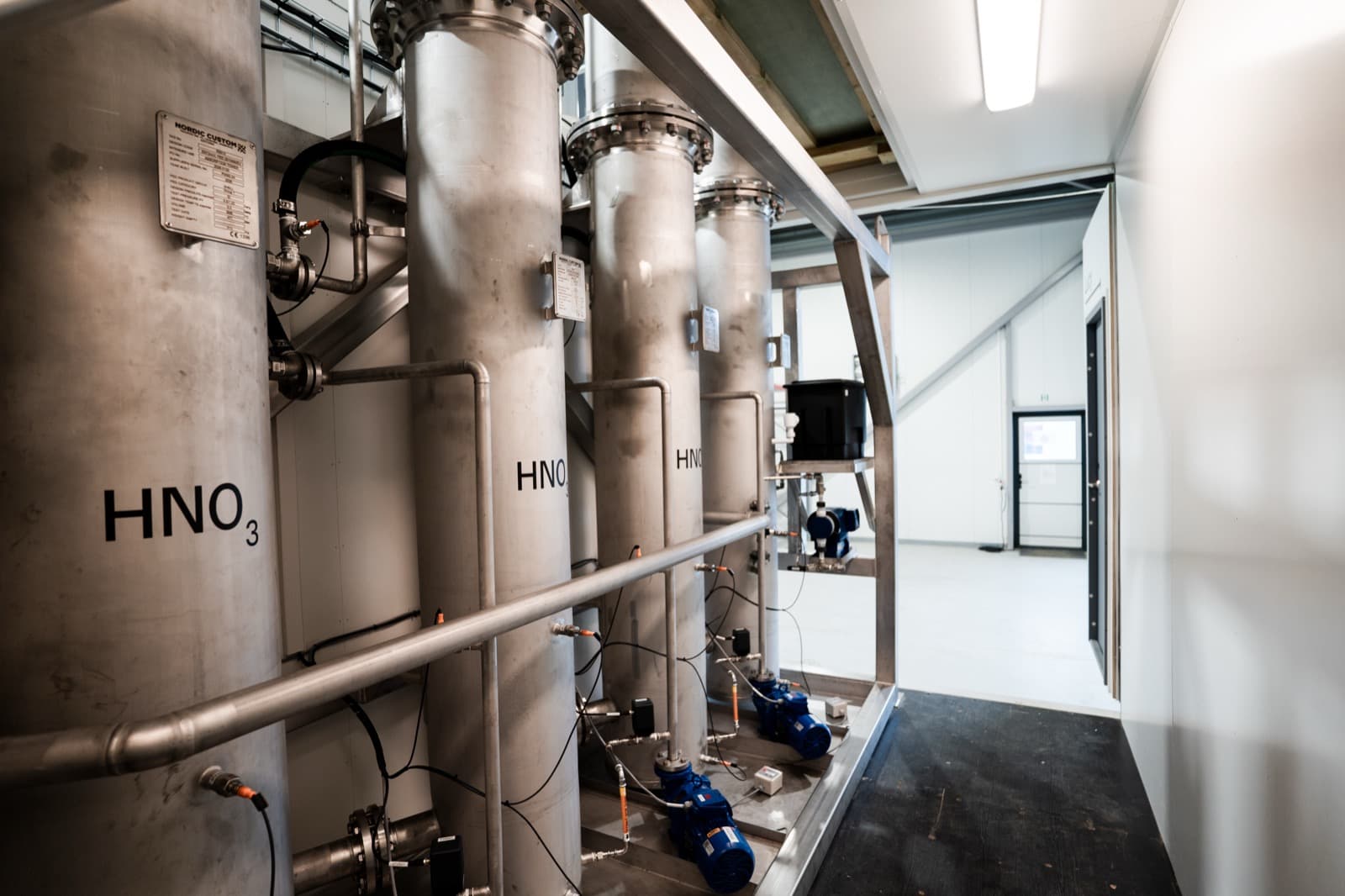 Four stainless absorption columns stencilled HNO₃, with their pumps and pipework, inside a nitric acid unit