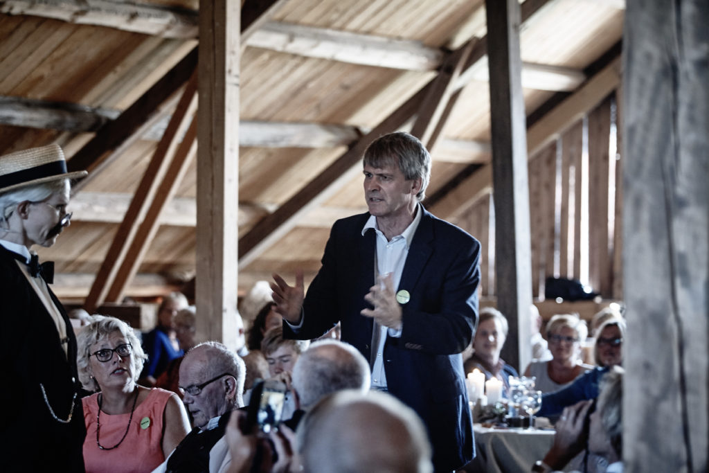 The dialogue between Professor Birkeland and Mr. Ingels starts amidst lunch guests in the barn at Strand gard in Norway